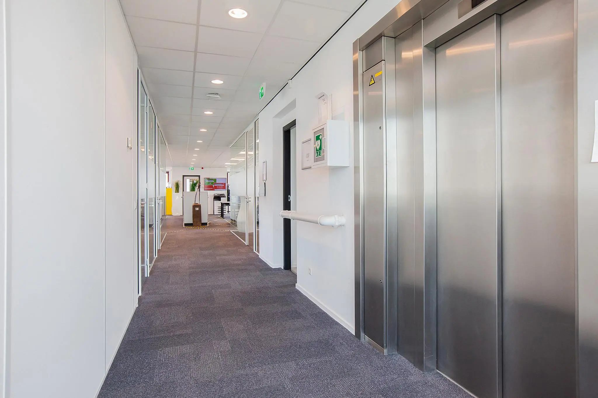 Moderne kantoorhal in gebouw aan de Laan der Verenigde Naties met liftdeuren en glazen kantoormuren.